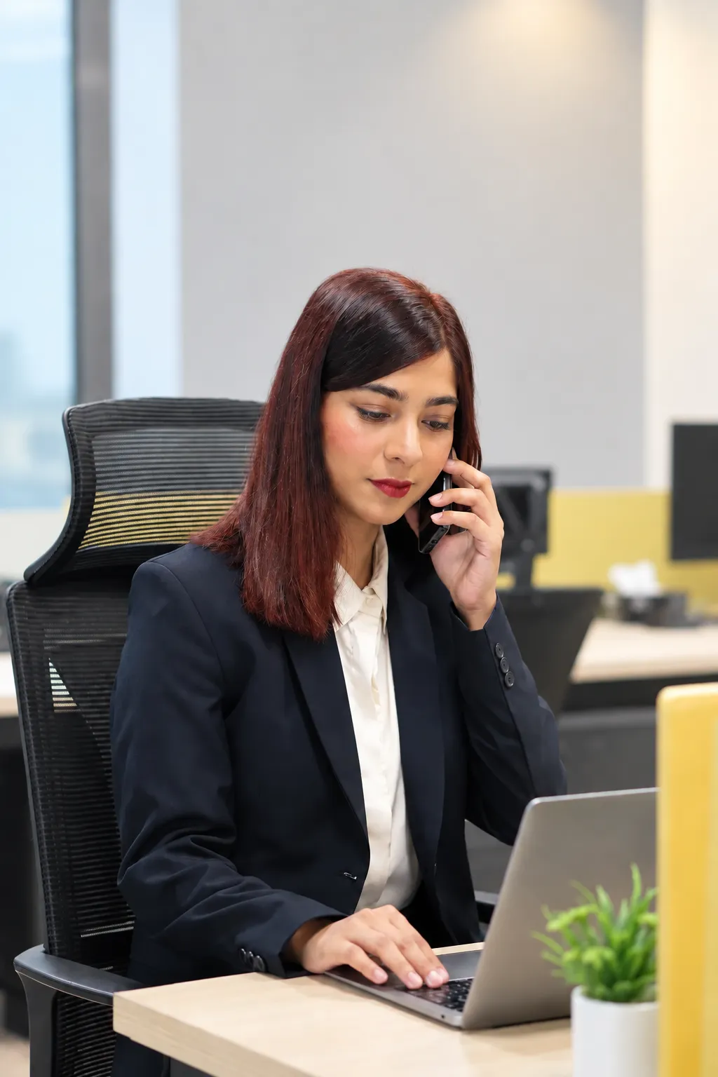 An accountant at a desk taking a phone call while working on a laptop.